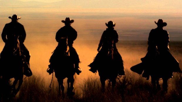 Slow Motion Panning Shot Of Four Cowboys Riding Horses.