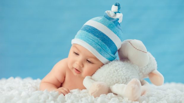 A baby boy lying on clouds with sheep toy images.