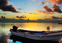 Peaceful sunset over calm water with boat and colorful sky.