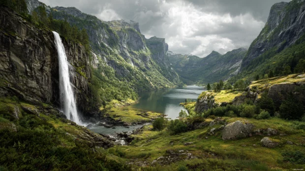 Panoramic waterfall desktop wallpaper showing a cliffside cascade pouring into a serene lagoon under cloudy sky.