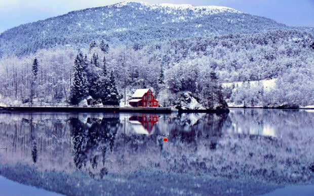 Snowy mountain landscape with Winter Wonderland forest and red house by the lake reflection