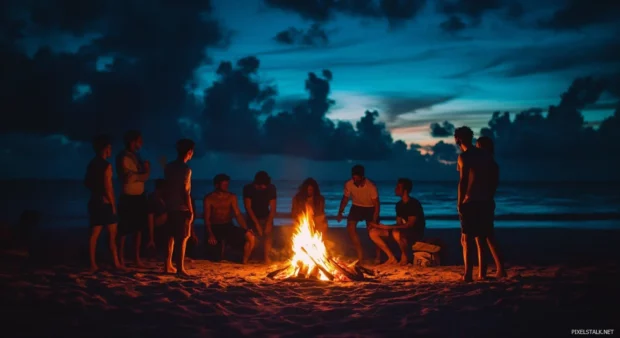 A group of friends gathering around a bonfire on a beach at night.