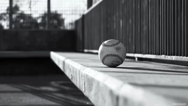 A baseball balanced on the edge of the dugout bench in monochrome.