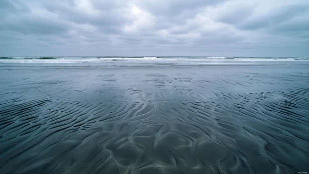 A beach at low tide with expansive sandy flats and distant wave.