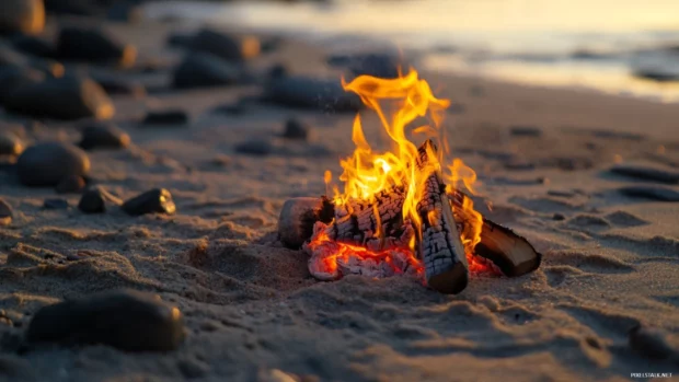A beach bonfire burning brightly as the sun rises, casting a warm glow on the surrounding .