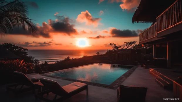 A beachside hotel with a swimming pool and lounge chairs, overlooking the ocean as the sun rises.