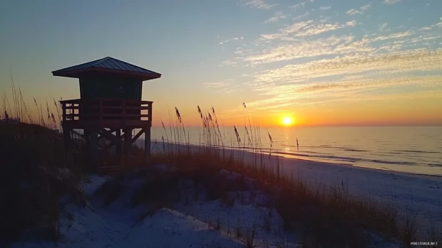 A beachside lifeguard tower silhouetted against a stunning sunrise, with the ocean stretching to the horizon.