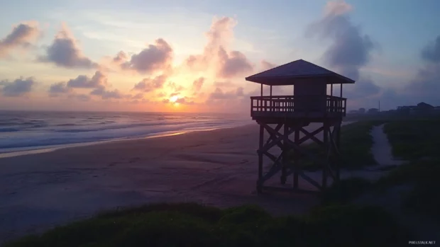 A beachside lifeguard tower silhouetted against a stunning sunrise, with the ocean to the horizon.