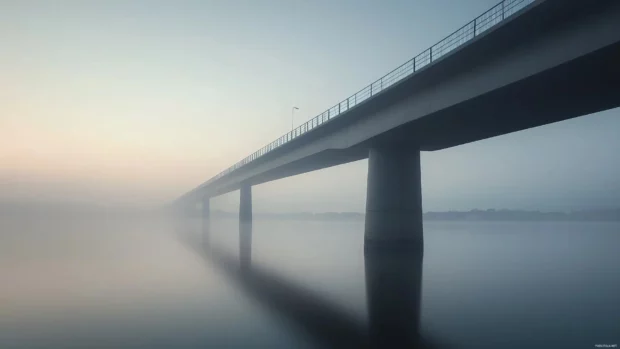 A bridge spanning over a calm river with the city faintly visible on the horizon.