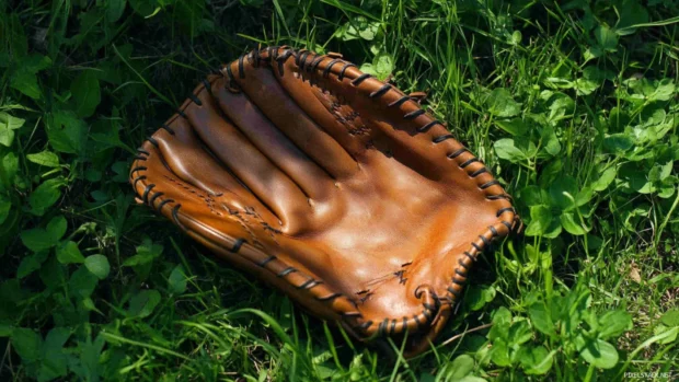 A classic leather baseball glove resting on fresh green grass during golden hour, Vintage leather baseball glove wallpaper.