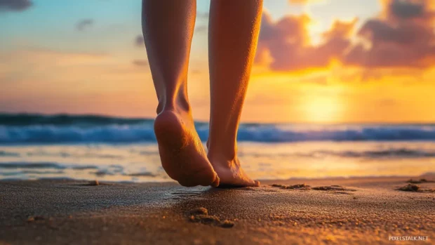A close up of a person feet walking on the sand at sunset, with the ocean and colorful sky in the background.