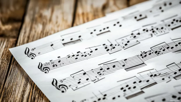 A close up shot of beautifully handwritten sheet music spread across a rustic wooden table, with delicate shadows and warm light illuminating the notes and lyrics.