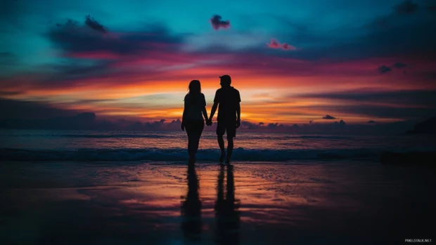 A couple walking hand in hand along the beach at sunset with the ocean.
