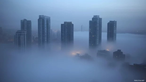 A foggy city skyline in the early morning with only the tallest buildings visible.