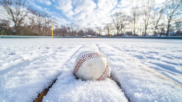 A frozen baseball field in winter, with snow covering the bases and frost on the dugout benches .