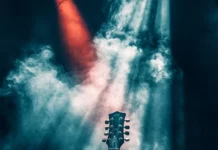 A guitar neck emerging from smoky stage light with visual depth inspired by Guitar silhouette wallpaper for iPhone.