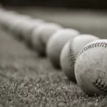 A line of baseballs on the grass in grayscale perspective.