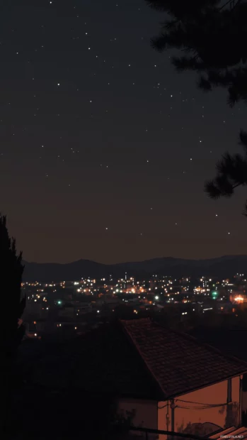 A peaceful night sky overlooking a city skyline, with stars shining brightly despite the faint glow of urban lights.