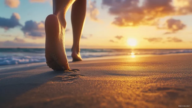 A person feet walking on the sand at sunset with the ocean .