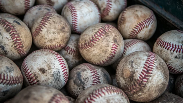 A pile of baseballs in a dugout, showing different levels of wear and tear.