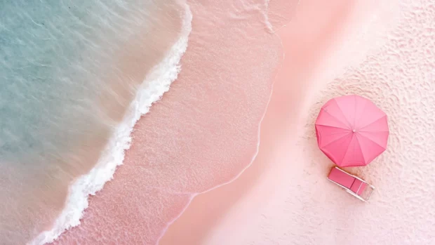 A pink beach with minimalist design, featuring a pink umbrella, chair, and ocean.