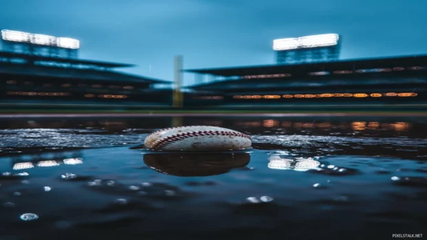 A rain soaked baseball field, puddles forming in the dirt and reflections of stadium lights in the water .
