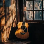 A serene image of an acoustic guitar leaning against a rustic wooden wall, with warm sunlight streaming through a nearby window.