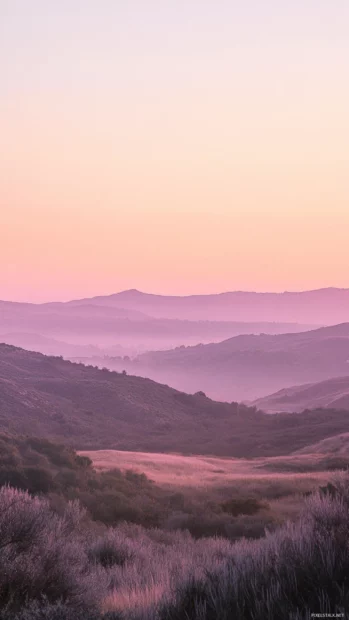 A soft pink glow of sunrise paints the landscape in warm tones.