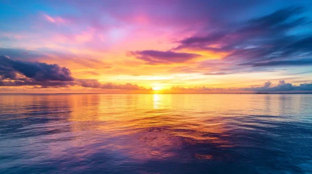 A vibrant sunrise over a calm ocean, with colorful clouds reflecting on the water surface .