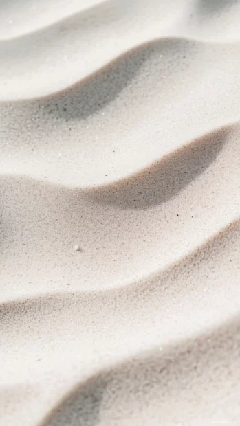 An aesthetic beach with seafoam patterns on sand in soft morning light.