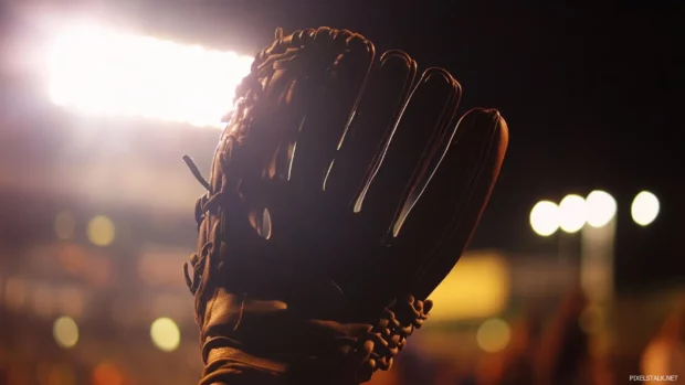 Baseball glove under bright stadium lights with blurred crowd.