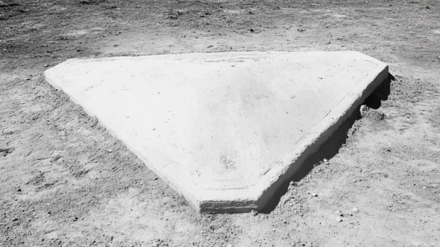 Baseball resting at the corner of home plate in monochrome.
