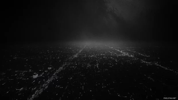 Black city shrouded in shadows with only distant lights visible.