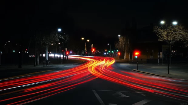 City intersection at night with long exposure capturing light trails from passing cars.