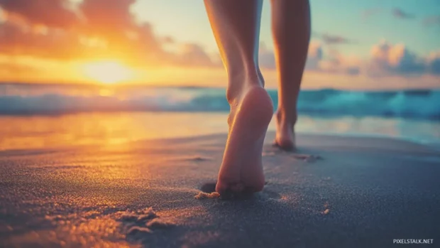 Close up feet on sand, sunset and ocean view behind.