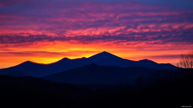 Early light silhouettes the mountain peaks against a brightening sky.