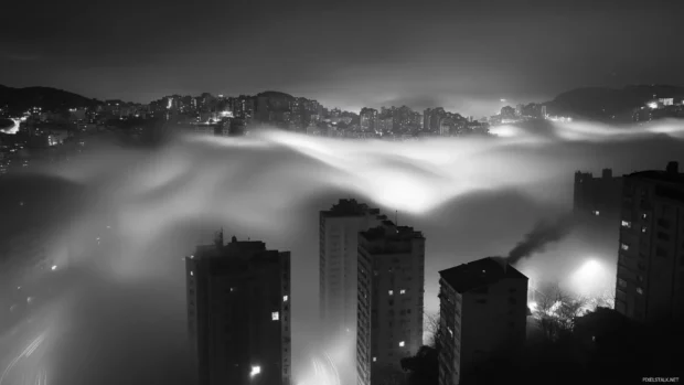 Fog drifting over buildings in a black and white city wallpaper night scene.