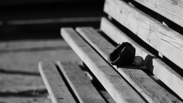 Glove and baseball placed on wooden bleachers in black and white.