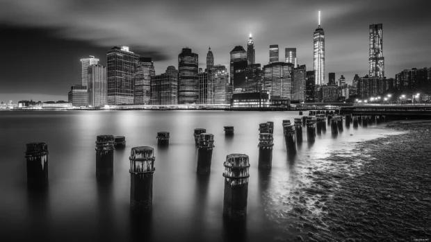 Glowing skyscrapers of dramatic Manhattan skyline at night, city lights reflected in Hudson River.
