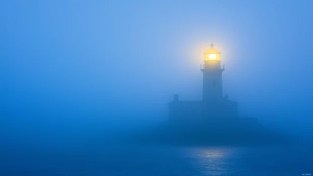 Lighthouse beacon shining through morning fog at dawn.