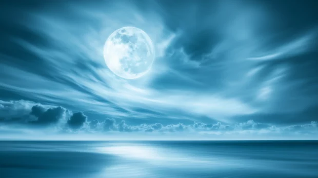 Luminous full moon through thin clouds, casting glow on the calm ocean.