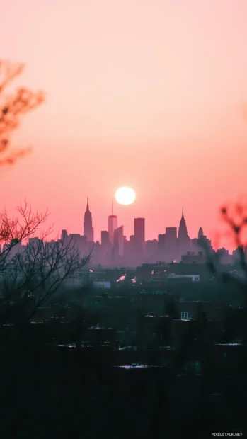 New York City skyline silhouette set against a soft pink and orange sunset.