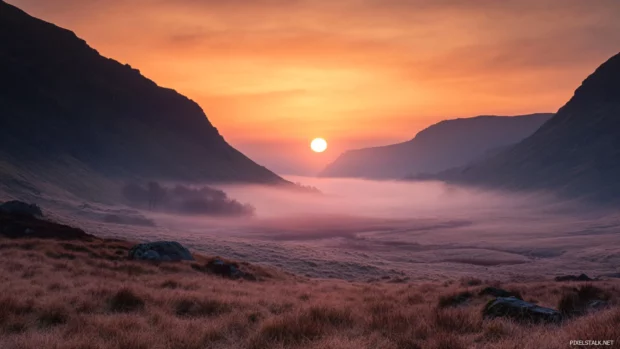 Pale sun rising over a fog laced valley.