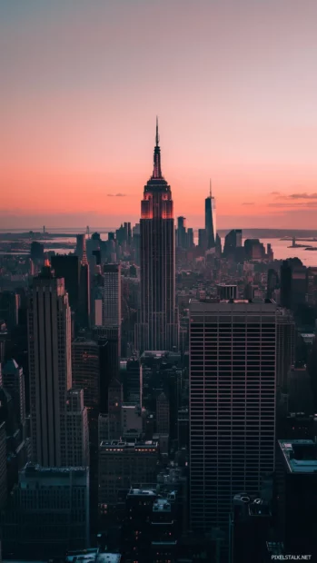 Silhouette of the New York City skyline against a soft pink and orange sunset.