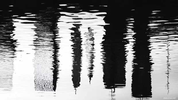 Skylines ripple gently in river reflection grayscale panorama.