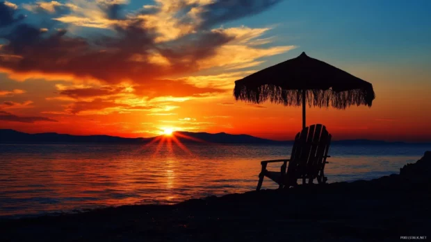 Sunset over ocean with beach chair and umbrella in silhouette.