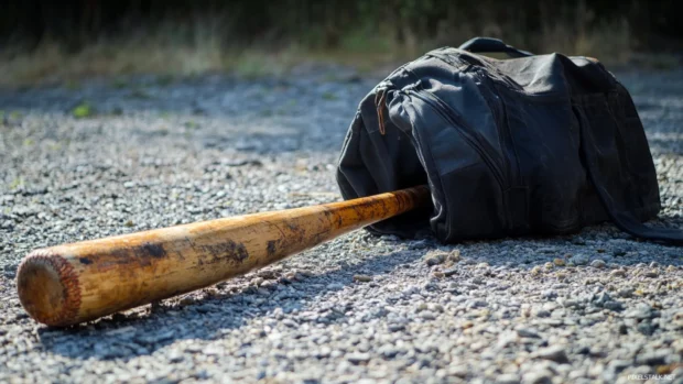 Worn baseball bat next to a sports bag on gravel.