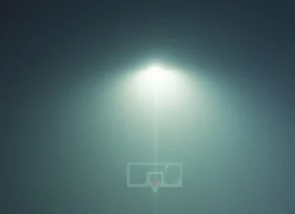 A basketball rests at the three point line as fog rolls across the court.