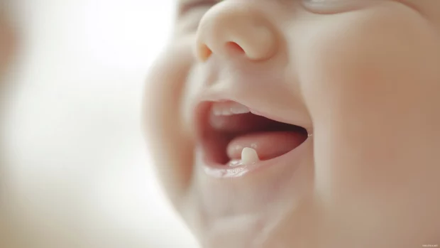 A close up of a baby boy face with a gentle laugh, showing tiny teeth and soft, chubby cheeks.