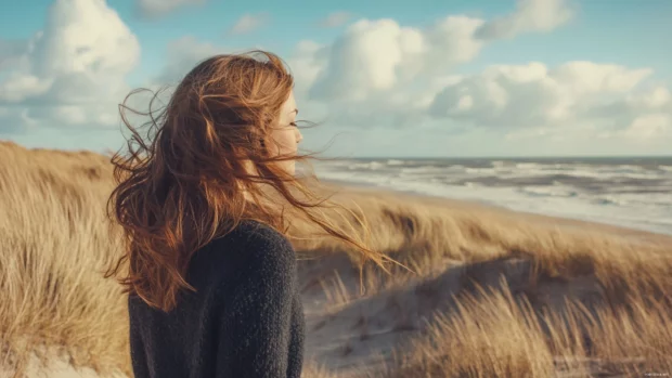 A girl with long flowing hair standing on a windy beach, looking at the horizon, cinematic lighting.